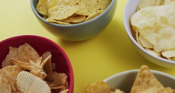 Close up of four bowls full of variety of chips on yellow surface