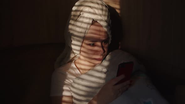 Close Up of Young Woman with Towel on Her Head Browsing Smartphone in Dark Room