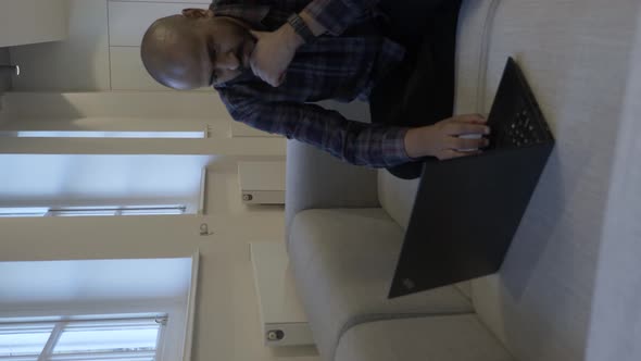 UK Asian Male Using Laptop Sitting On Office Sofa. Vertical Video, Locked Off