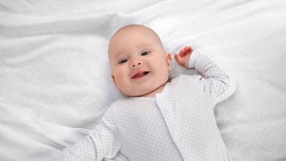 Top View Portrait of Adorable Little Baby in Sliders Lying on White Sheet