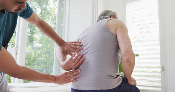 Slow motion shot of male caregiver examining retired senior man's spine at nursing home