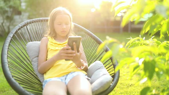 Happy kid girl playing game on mobile phone in the park outdoor