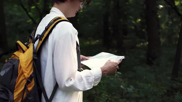 Traveler Girl Looks At Map While Walking Along Road. Tourist With Backpack Is Looking For Way