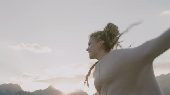 Happy woman with dreadlocks jumping and having fun in Field under sunlight in evening.