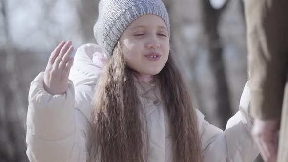 Close-up Portrait of Mischievous Little Girl Gesturing and Rubbing Eyes Outdoors. Disobedient