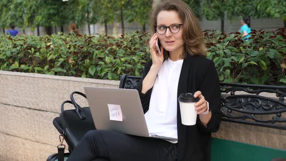 Businesswoman With Laptop On Coffee Break Speaking On Smartphone