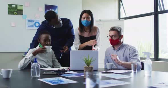 Office colleagues wearing face masks using laptop together in meeting room at modern office