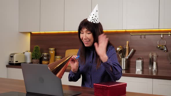 Aged Woman in Party Hat Opens Red Gift Box and is Surprised in Home Kitchen