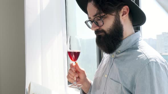 Pleased Bearded Man Drinking Red Wine While Reading a Book at Home