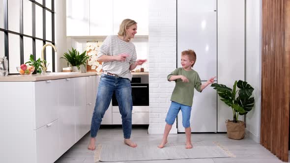 Excited Mom or Babysiter and Kid Boy Jumping Dancing Laughing in Modern Scandinavian House Kitchen