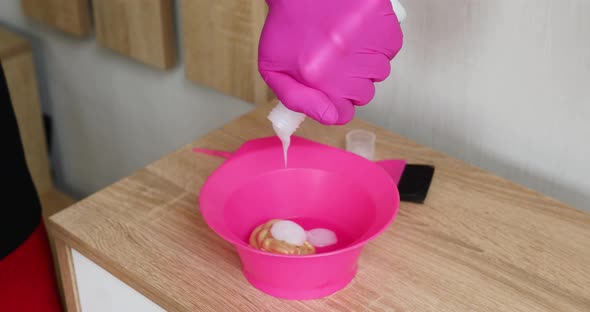 Slow motion Unrecognizable female wpman in pink glove squeezing pigment in bowl