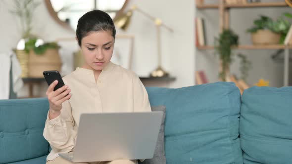 Indian Woman Working on Smartphone and Laptop on Sofa 