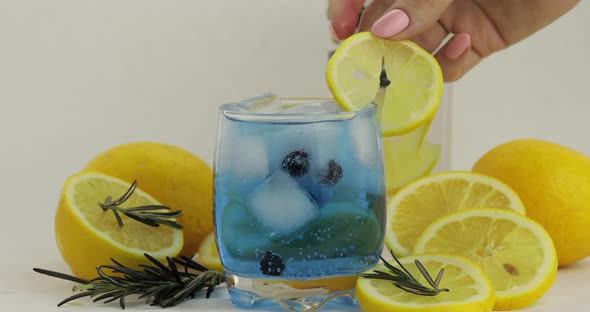 Adding Lemon Slice in a Glass with Soda Lemonade Blue Cocktail