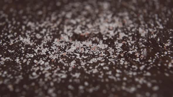Crystals of ground Himalayan salt crumble in slow motion on the dark wooden surface