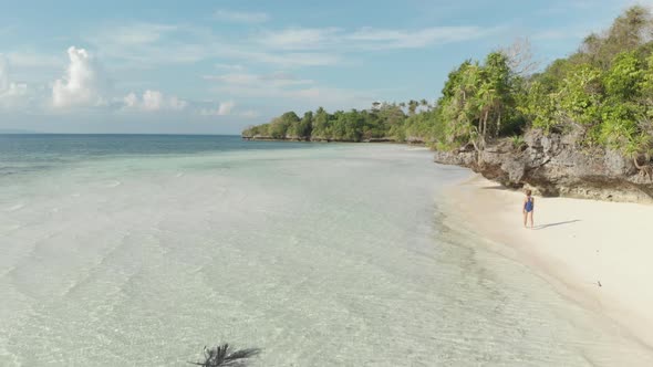 Aerial: woman walking on tropical island turquoise water white sand beach