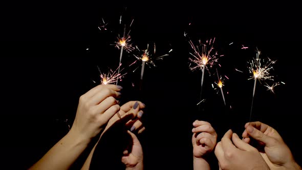 Close-up of Hands Holding and Waving Bengal Fire Burning Sparklers in Front of Black Background