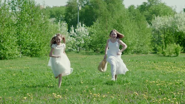 Two Girl Friends Running on Flowering Meadow in Green Park at Sunny Day