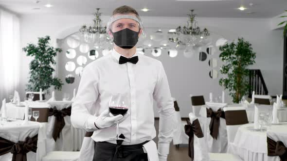 Waiter in a Protective Mask with a Glass of Red Wine in His Hands