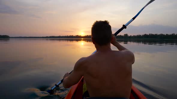 A Man Kayaks on a Calm River Towards the Sunset