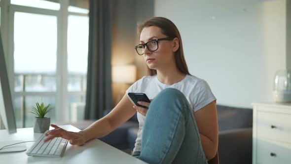 Casually Dressed Woman Working with a Computer and Smartphone at Home in a Cozy Environment
