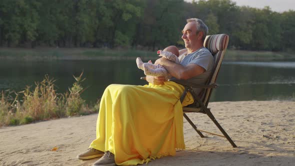 Grandfather Holding Newborn Baby Granddaughter Outdoors.