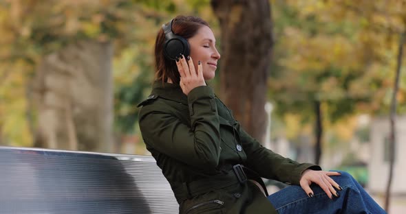 Woman Listening Audiobooks Wearing Headphones Sitting on the Bench in a Park