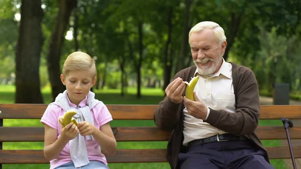 Grandfather and Boy Eating Bananas in Park, Snacking Outdoors, Healthy Food