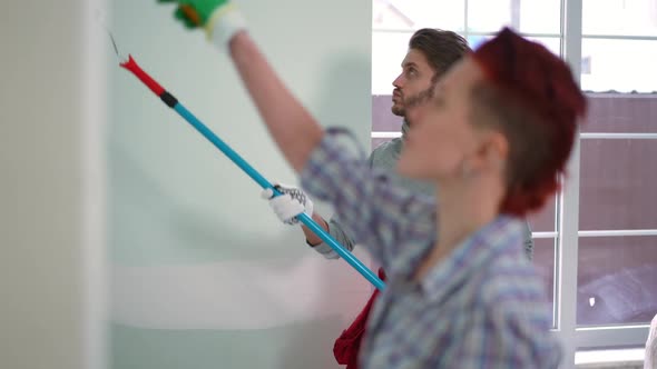 Side View Concentrated Handsome Man Painting Walls with Blurred Woman at Front