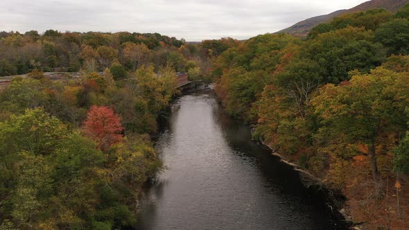 An aerial shot of the colorful fall foliage in upstate NY. The camera dolly in over a black river wi