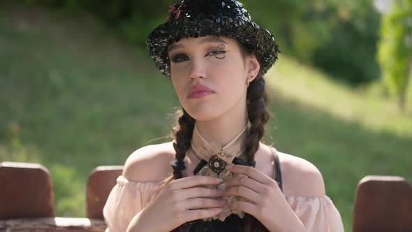 Slim Charming Young Woman in Steampunk Dress with Pigtails Looking at Camera Checking Makeup