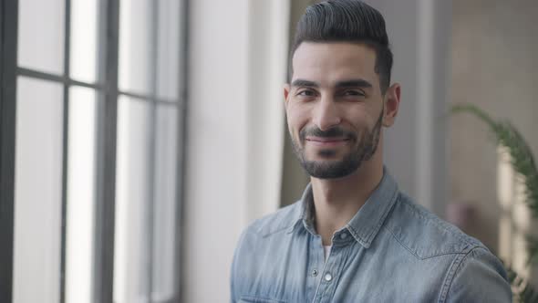 Portrait of Handsome Smiling Young Middle Eastern Man Looking at Camera and Looking Out the Window