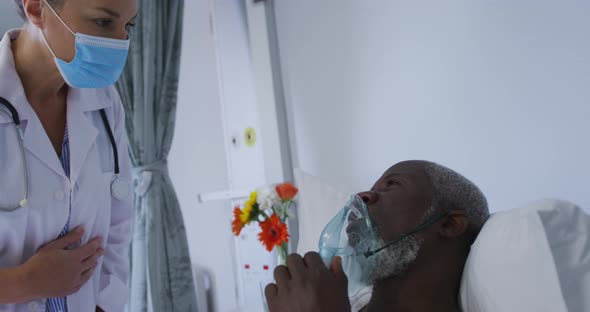 African american male patient in hospital bed wearing oxygen mask talking to doctor