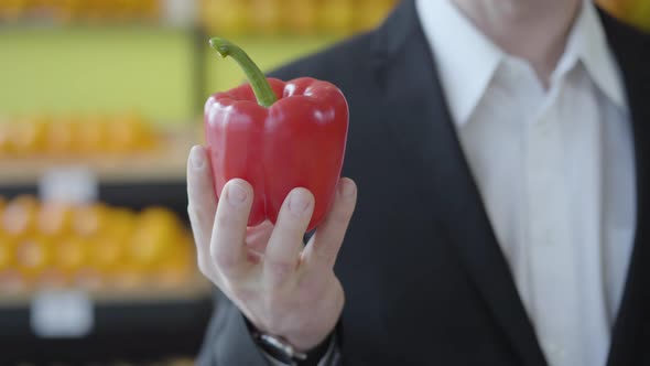 Close-up of Male Caucasian Hand Holding Red Fresh Bell Pepper in Grocery. Unrecognizable Man Showing