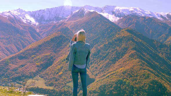 beautiful blonde takes photos or videos of a landscape in the autumn mountains.