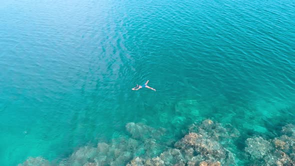 Aerial slow motion: woman snorkeling on coral reef tropical sea from above