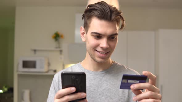 Smiling man holding credit card and mobile phone while shopping online at home