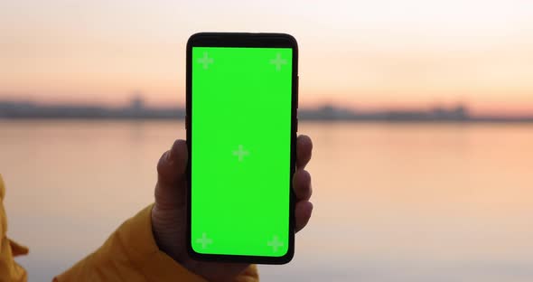 Man Shows Green Screen in Smartphone Near River