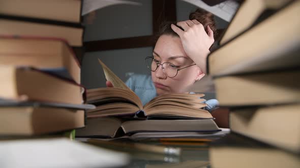 A young girl with glasses lazily leafs through a textbook late at night