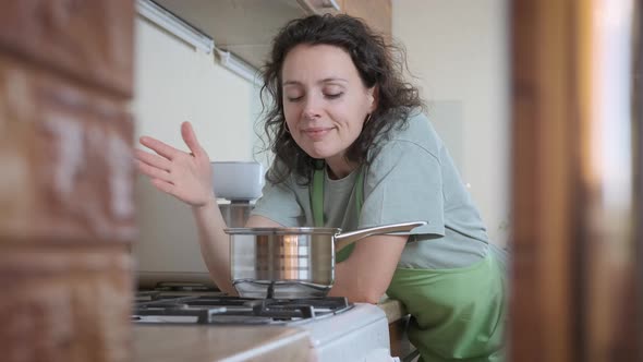 A woman at the stove sniffs the aroma of food.