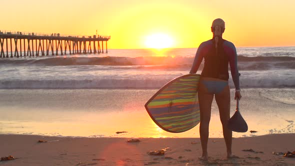 A silhouetted portrait of woman sup stand-up paddleboard surfing at the beach at sunset