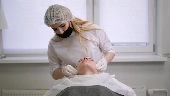 Doctor Beautician Removes White Cream From the Face of His Patient Lying