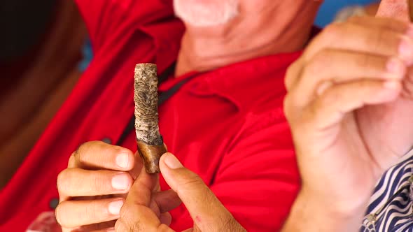 Older gentleman with shaky hands holing and smoking a nearly finished cigar in the Caribbean