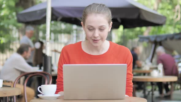 Young Woman Celebrating on Laptop Sitting in Cafe Terrace