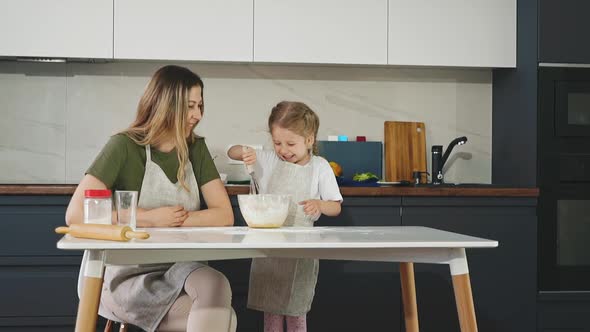 Happy Mother with Daughter Mix Dough at Table in Kitchen