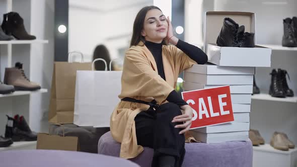Wide Shot Satisfied Female Client Sitting in Shoe Shop with Lot of Boxes Smiling