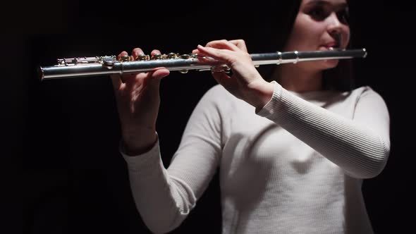 Young Female Student Plays Studio Flute with Dark Background Front View