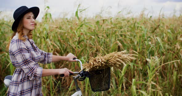 Woman in Hat Walking with Bicycle and Wheat Ears in Basket