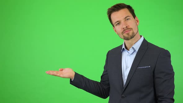 A Young Handsome Businessman Puts Out a Hand with a Product, Smiles and Nods - Green Screen Studio