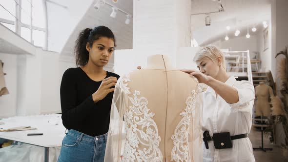 Females Tailors are Working on Wedding Dress Hanging on Mannequin Measuring and Pinning It Up