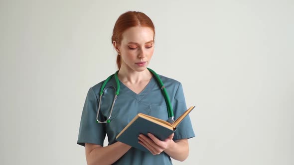 Medium Shot Portrait of Female Doctor in Green Uniform with Stethoscope Reading Medical Book